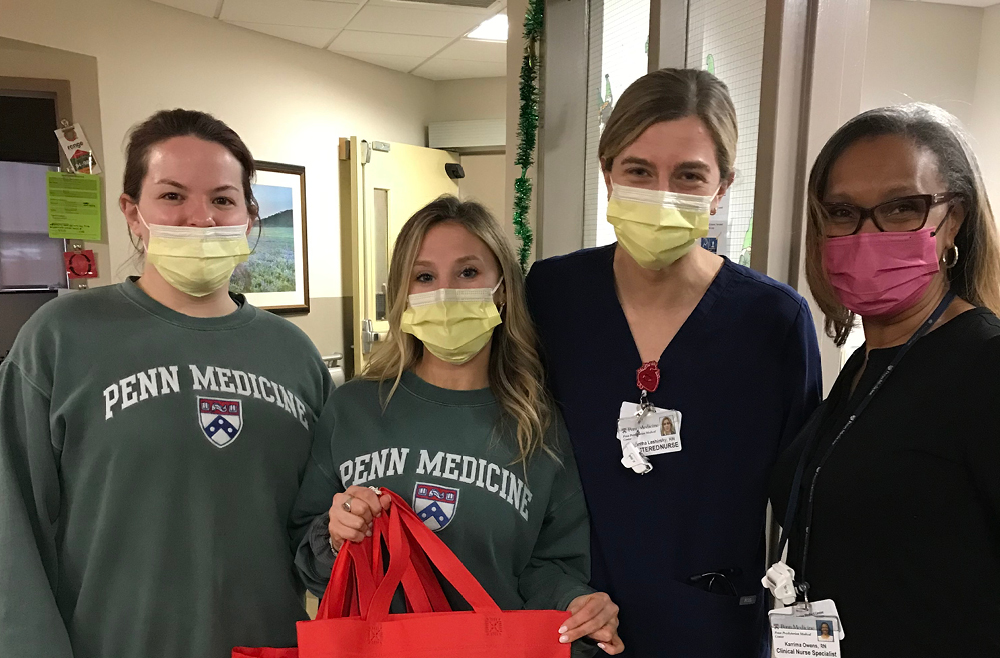 Four hospital workers, one holding red bags of donated toiletries for patients.